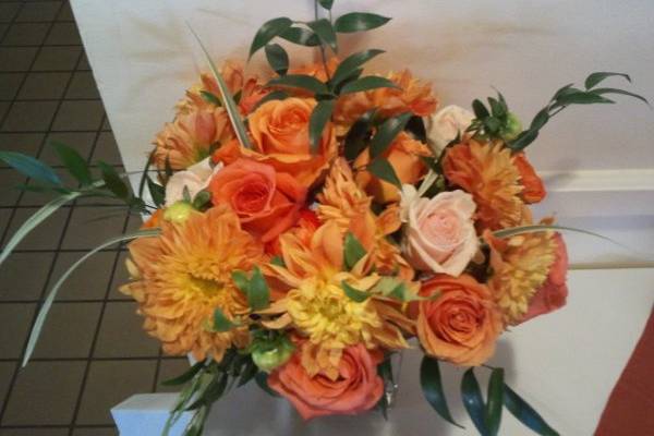 Close-up of arrangement #1. Orange, cream, and red-gold roses, orange dahlias, orange ranunculus, and greens.