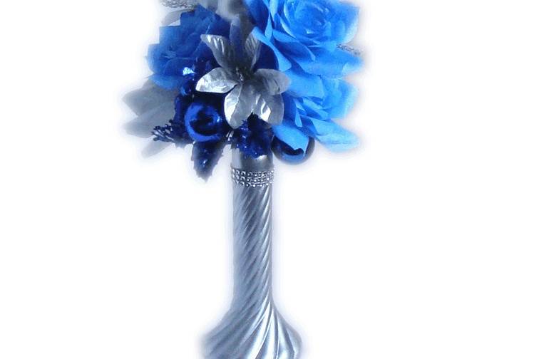 A silver glass vase filled with shimmering blue and silver handmade coffee filter paper flowers, glass Christmas ornaments and silver shimmering and glittered silk leaves. Around the top of the vase is silver rhinestone ribbon mesh.