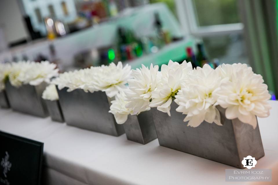 Bright white dahlias in sleek metal containers adorn the three sided bar.