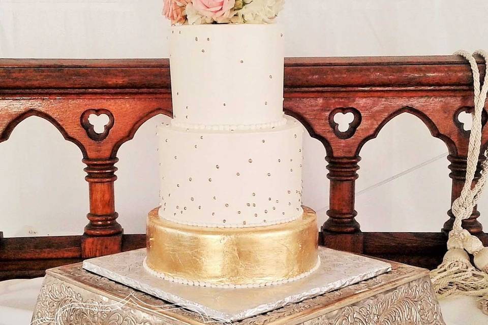 a simple and elegant white buttercream wedding cake with edible gold details and fresh flowers