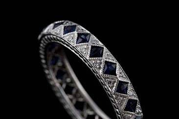 This stylish art deco inspired platinum wedding ring contains 22 French cut blue sapphires (Approx. 1Cttw) set in milgrained bezels and 44 micro pave set round brilliant diamonds (G color and VS clarity approx. 1/3Cttw). This band is 3.8 mm wide and 2.3mm tall. Sides have detailed design and top edges are milgrained. This band is available in all sizes. Please allow 2- 3 weeks to complete the order.