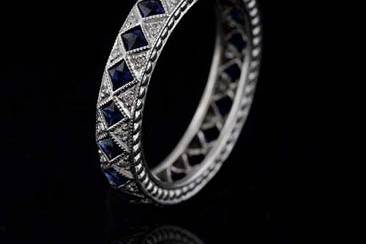 This stylish art deco inspired platinum wedding ring contains 22 French cut blue sapphires (Approx. 1Cttw) set in milgrained bezels and 44 micro pave set round brilliant diamonds (G color and VS clarity approx. 1/3Cttw). This band is 3.8 mm wide and 2.3mm tall. Sides have detailed design and top edges are milgrained. This band is available in all sizes. Please allow 2- 3 weeks to complete the order.