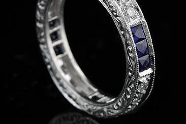 This gorgeous ,art deco design, platinum eternity band contains 12 French cut natural blue sapphires (Princess cut - approx. 1cttw) channel set and 12 round brilliant diamonds pave set (G-H color and VS clarity, approx. .35Cttw). This vintage inspired eternity ring is 3.6mm wide and approx 2mm tall. It is hand set, edges are milgrained and sides are engraved. Also available with rubies and diamonds (please contact us for more information). Please allow 2- 3 weeks to complete this order.