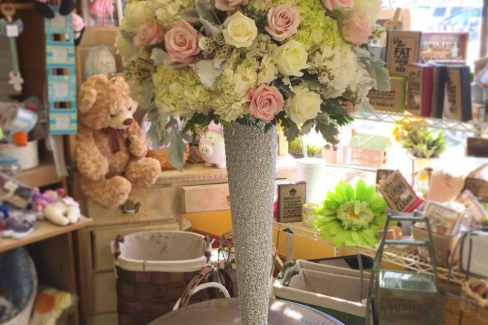 Lush ball arrangement on top of diamond pilsner vase designed with dusty miller, white hydrangea , sweet eskimo roses and white polar star roses.
