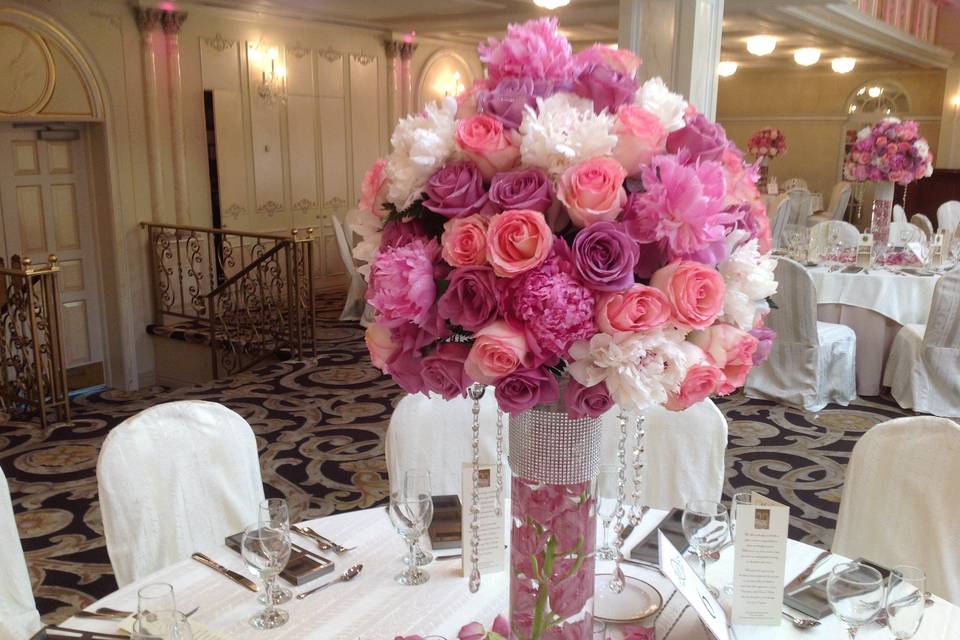 Lush ball designed with pink peonies, pink roses, and lag roses  and white peonies on top of cylinder vase with diamond band and hanging crystals .