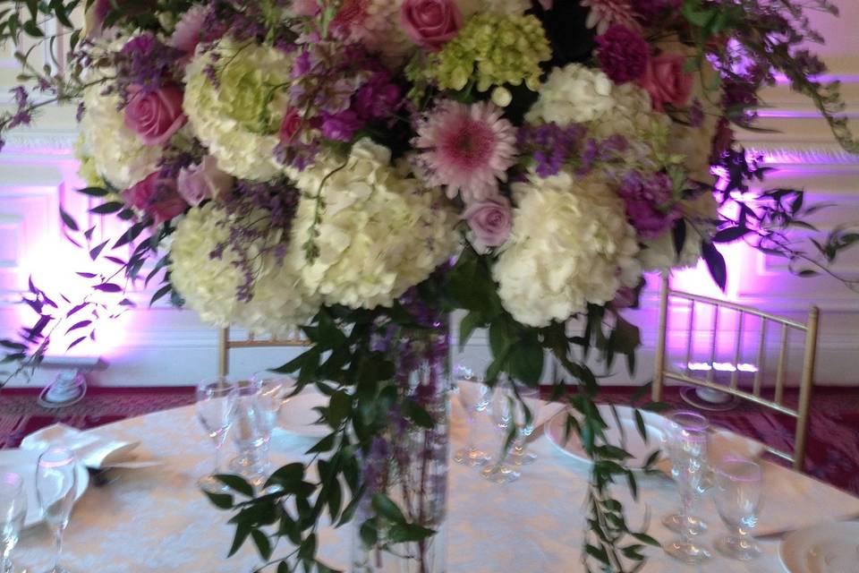 Lush ball designed with pink peonies, pink roses, and lag roses  and white peonies on top of cylinder vase with diamond band and hanging crystals .