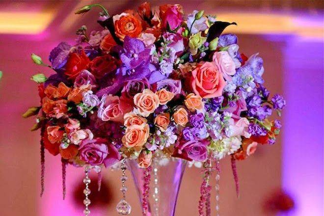 Wedding arrangement designed with black magic roses,red callas , green hanging amaranthus ,and green hydrangeas on top of clear glass pilsner vase .