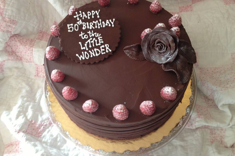 Chocolate sour cream cake layered with raspberry buttercream and fresh berries.  Frosted in dark chocolate ganache, garnished with fresh berries, a modeling chocolate rose and a Happy Birthday message plaque.