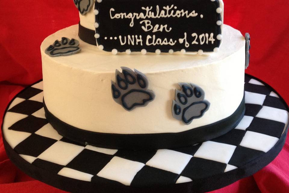 Graduation cake for UNH engineering student whose club built and raced a Formula car! Buttercream frosted cake features sugar paste wildcat paw prints, a fondant covered checkerboard base, a sugar paste Formula car and a plaque.