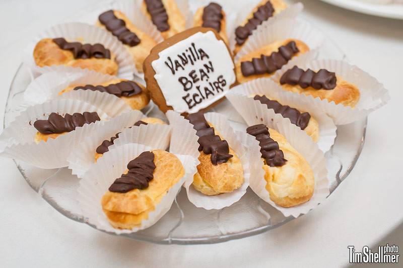 Miniature eclairs filled with vanilla bean pastry cream, topped with dark chocolate ganache ruffle.  Dessert label is entirely edible, made of gingerbread.
