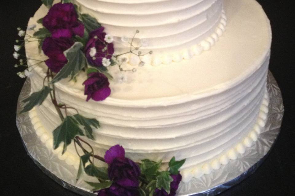 Elegant round wedding cake with ribbon swirl design and piped pearl border.  Lemon cake with strawberry buttercream filling and vanilla buttercream frosting.  Fresh flower decor.  Private home in North Conway, NH