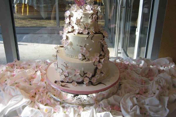 Cake is covered in sugar cherry blossoms with a chocolate branch going up the cake. Cake is a white chocolate cake filled with strawberries and cream