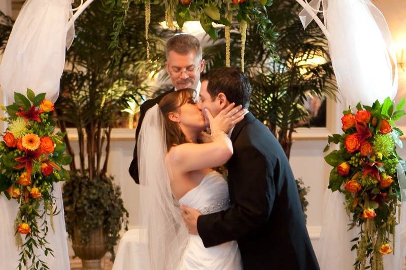 Traditional iron grillwork arch with tulle decoration for your ceremony. Flowers include orange gerberas, orange roses, green hydrangea, ruscus.www.tigerweddings.com