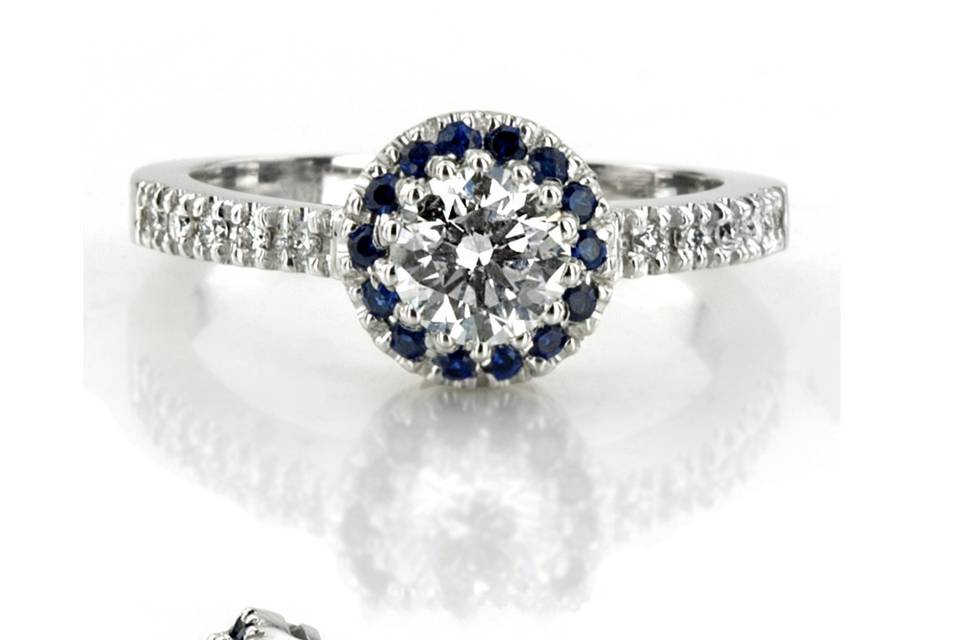 This classic halo engagement ring is furnished with sapphires and diamonds. Sapphires accent the center stone to bring out the beauty in it. Shank is bead set with diamonds to add to the sparkle of the engagement ring. Engagement ring is set with 16-1.3mm sapphires 0.16ct. tw. and 10-1.3mm diamonds 0.10ct. tw. This micro pave look engagement ring is available in 14k, 18k, platinum and palladium.