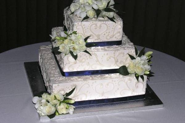 Elegant and beautiful, this 3-tiered ivory buttercream cake adorned with hand-piped scrollwork, fresh flowers, and ribbons to match your wedding theme colors are the perfect touch!