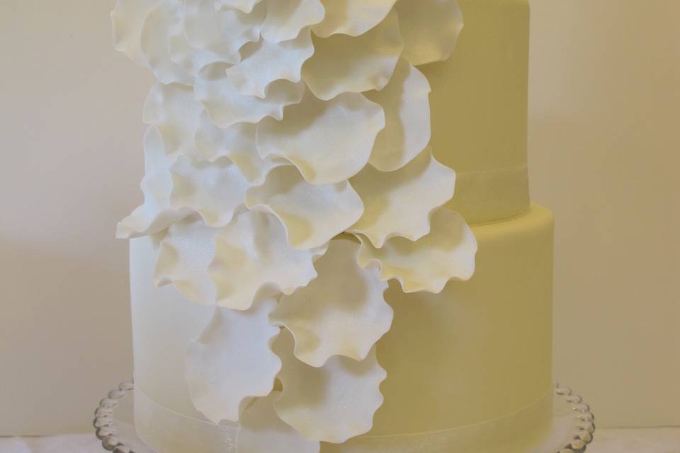 Fondant covered round tiers with a beautiful, large cascading handmade Sugar Rose which is brushed with edible Pearl Luster Dust.  Shimmery White Organza Ribbon trim on all tiers.  Displayed on our Vintage Candlewick Cake Stand.