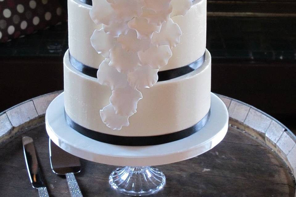 Four tiers covered in smooth American Butter Cream and adorned with a large, sugar paste Rose and Cascading Rose Petals highlighted with Gold Edible Luster Dust.  Ribbon Trim.  Cake Pedestal provided by the bride.  At Gloria Ferrer Caves and Vineyards, Sonoma.