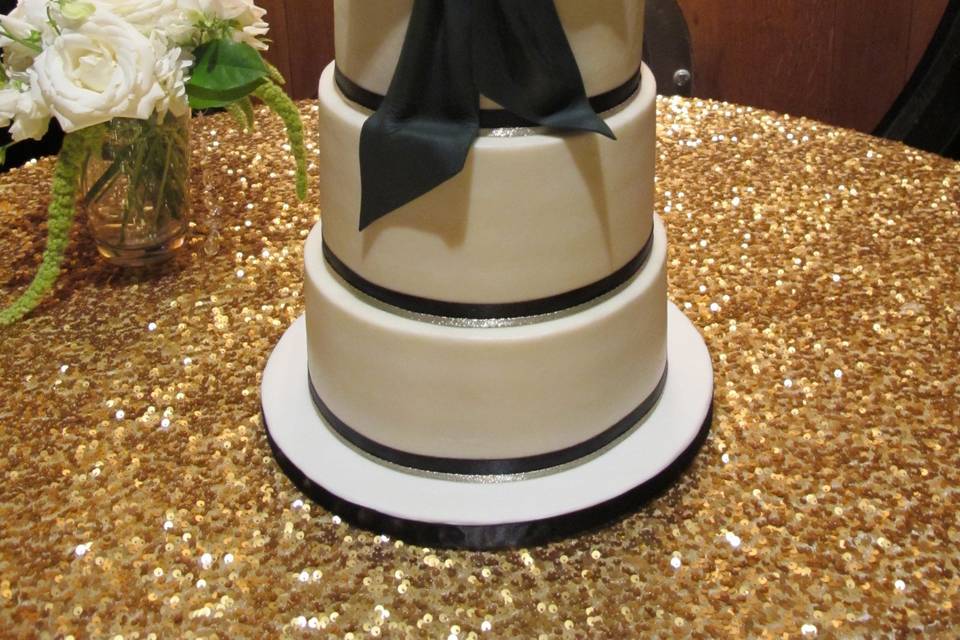 Four tiers frosted in American Butter Cream and adorned with a handmade Black Fondant Bow and Rhinestone Brooch.  Ribbon trim.  Topper provided by the bride and groom.  At V Sattui Winery in Napa.