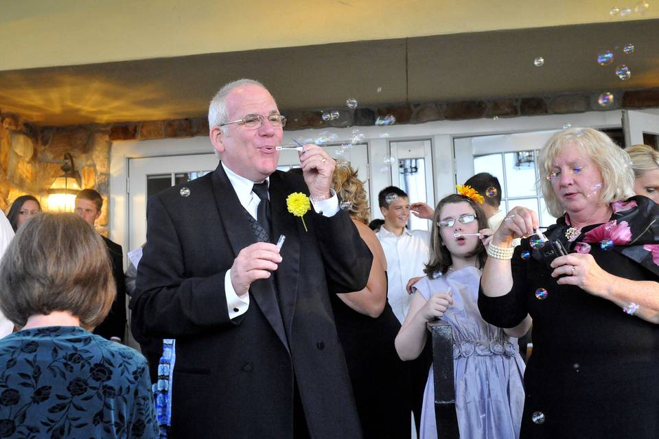 The bride's father blows bubbles with youthful enthusiasm for their reception exit.