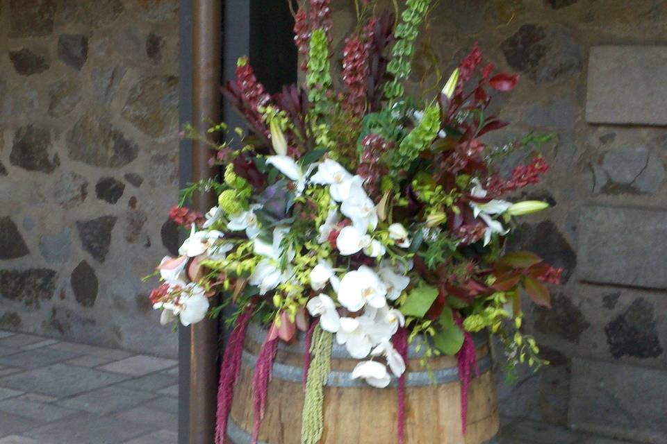 Wine barrel topper overflowing with lush green, white and burgundy flowers.