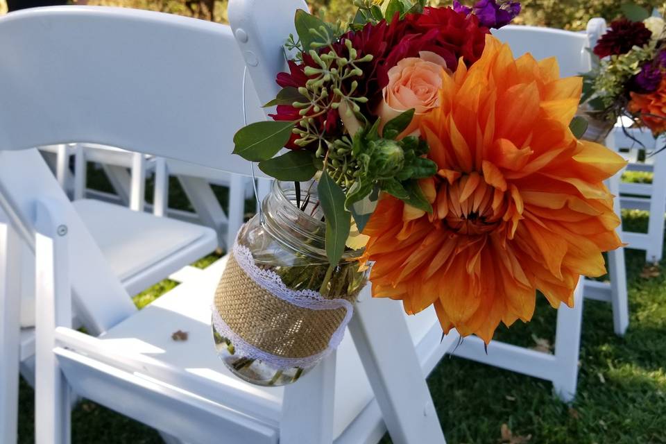 Aisle bouquet in mason jars, vibrant flowers in orange, purple and yellow.