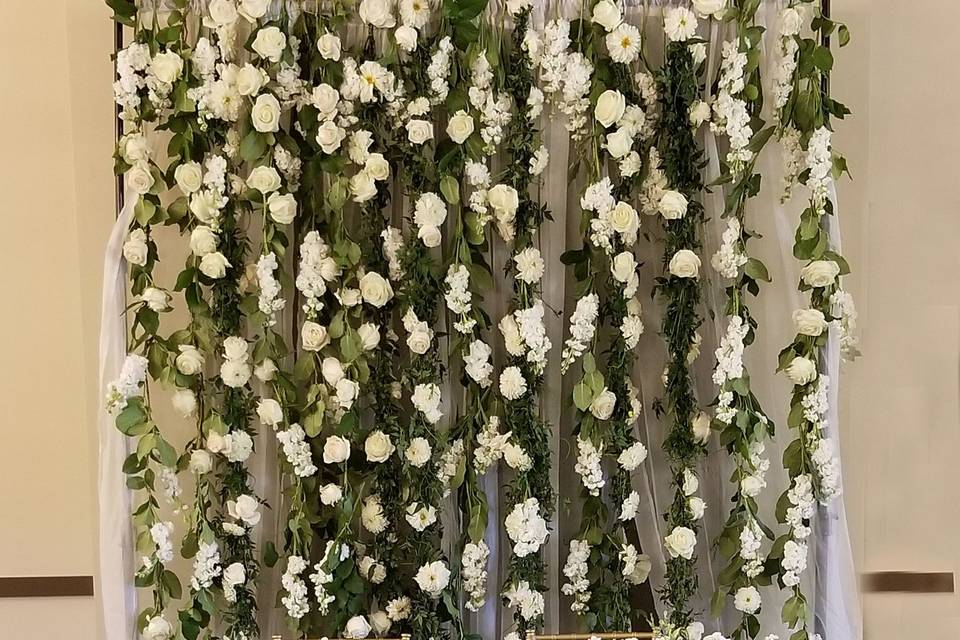 Sweetheart table backdrop, floral wall with hanging vines and white flowers. Table cascades in white, blush and greens.