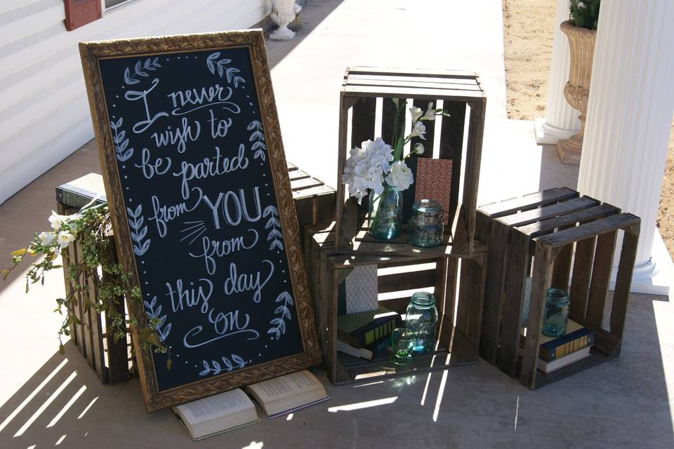 placed at entry- use of crates, aqua mason jars, books, floral, and a chalkboard for a Pride & Prejudice themed renewal wedding at the Arbuckle Wedding Chapel