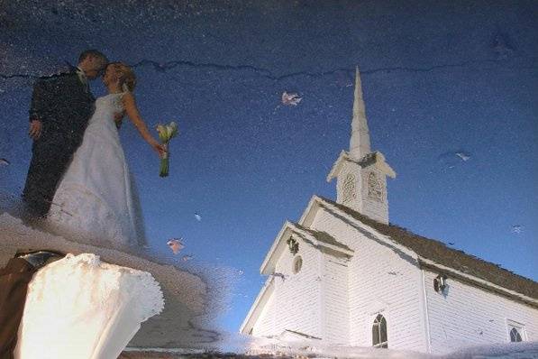 A bride and groom stop in front of a puddle outside the church where they got married on a cold winter day.