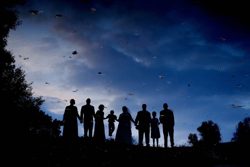 The wedding party are seen reflected in a pond at their Detroit area fall wedding at twilight.