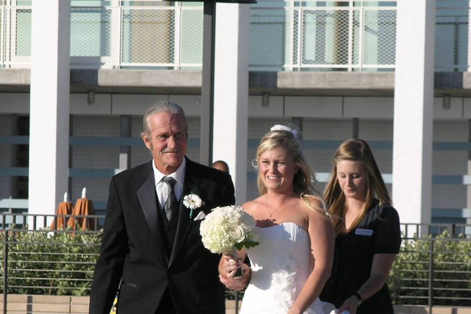 Bride down the aisle with The Father of the Bride.  She carries a white rose & stephanotis bouquet with jewels in the center of the stephanotis.