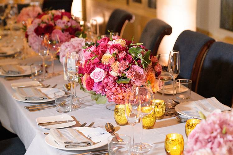 Long tables with multiple centerpieces of garden roses, hydrangeas and spray roses accented with gold votive candles.