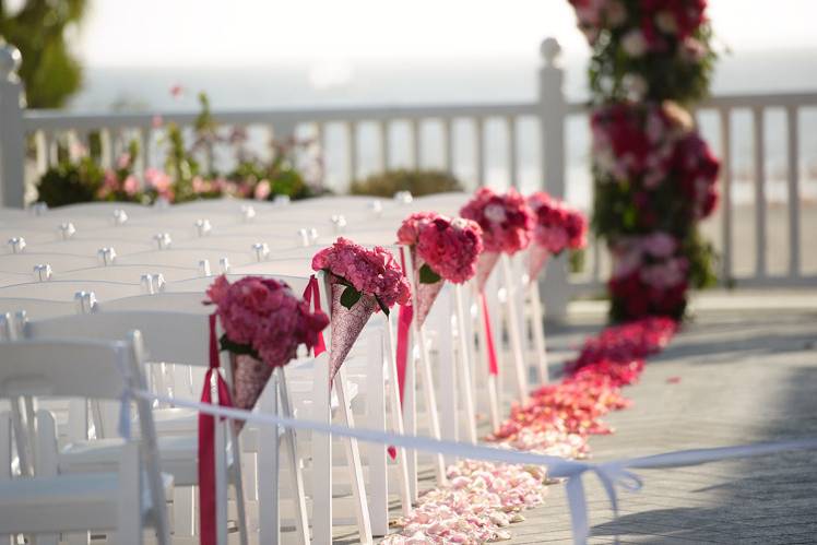 Aisle flowers in cones to match the color theme of this wedding. A romantic combination of roses and hydrangeas with pink paper cones accented with hot pink glitter floral design.