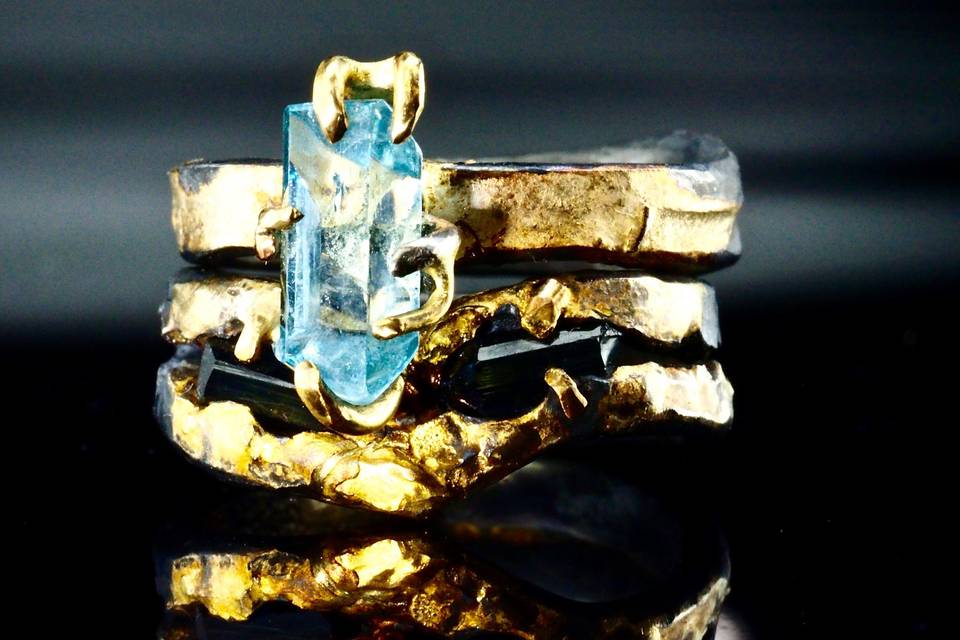 raw natural aquamarine crystal mounted in 18k gold claws on oxidized silver and fused 18k gold band stacked with a ring of two indicolite tourmaline crystals mounted in an oxidized sterling silver band fused with 18k solid gold