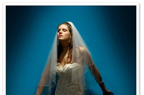 A stylish bridal photo of a bride with her wedding dress and veil poised against a blue wall.