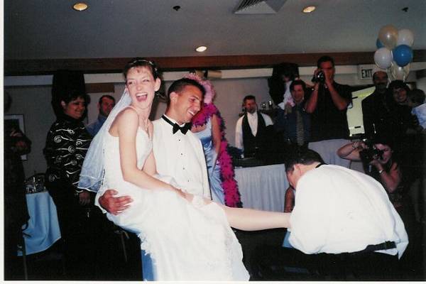 Groom getting garter while bride sits on best man's knee.