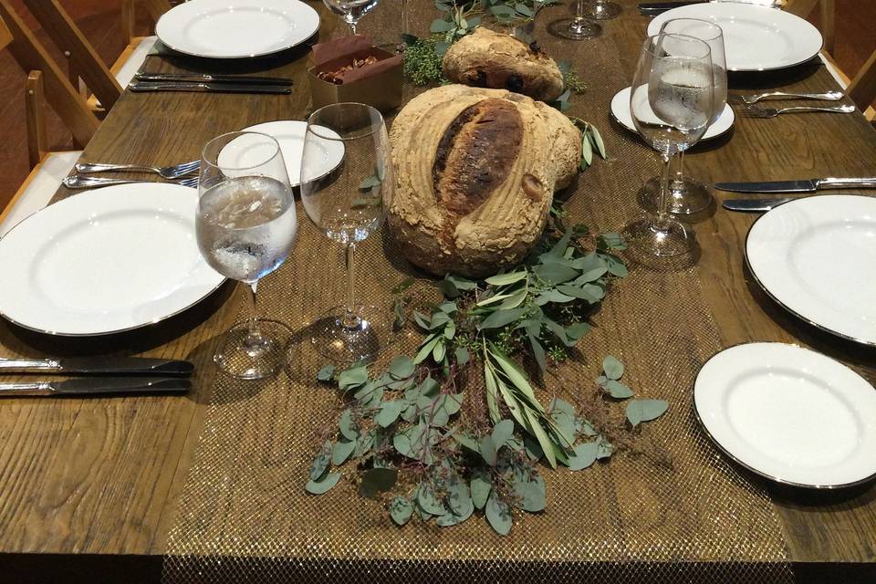 Kings table tablescape for family style service on beautiful hard wood tables with muted gold mesh table runners and eucalyptus greenery and sage napkins