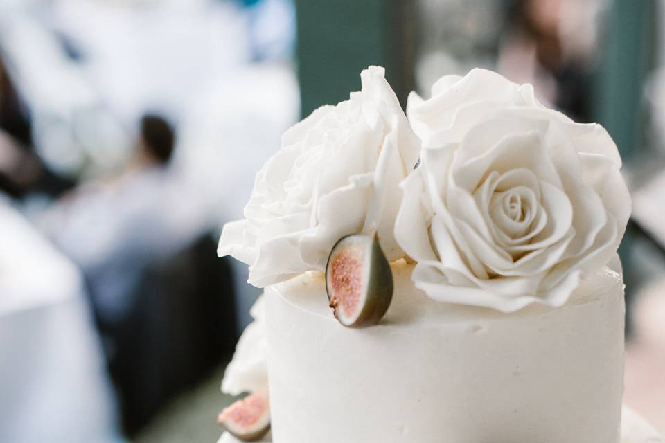 Dark chocolate cake filled with mascarpone cream and fleur de sel salted caramel, frosted in vanilla Italian buttercream, topped with salted caramel macarons, fresh figs, and sugar roses.