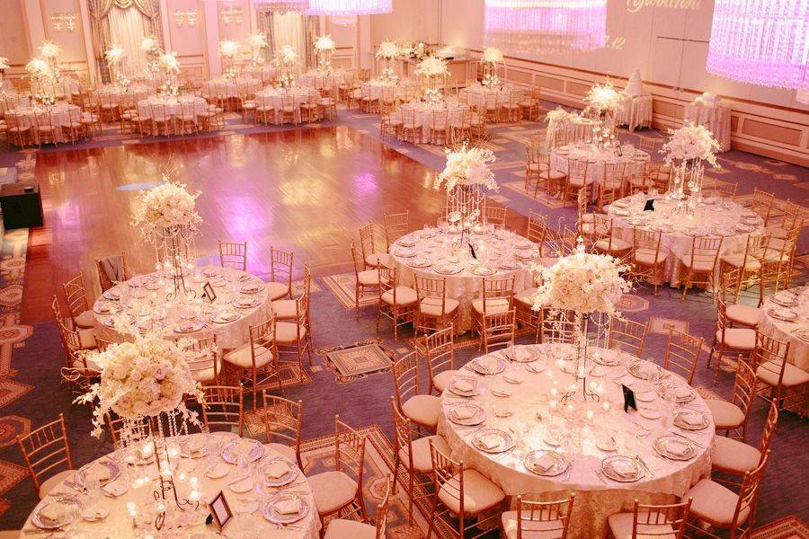 An over the top all white decor with blush lighting at The Grove featuring beautiful florals of roses, hydrangea and orchids with cascading glass bubble candles on crystal chain.