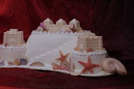 This sandcastle wedding cake if a free form design, featuring 2 white identical chocolate sandcastle toppers, plus a triple tower topper, and hand painted white chocolate seashells.