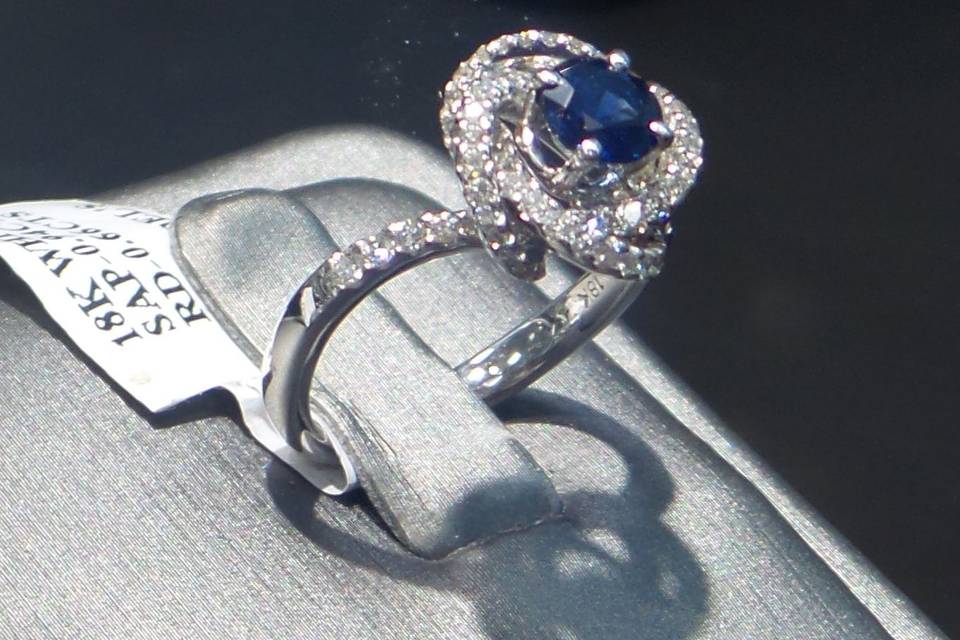 An eccentric sapphire center engagement ring with a spiraling diamond halo.
18K White Gold