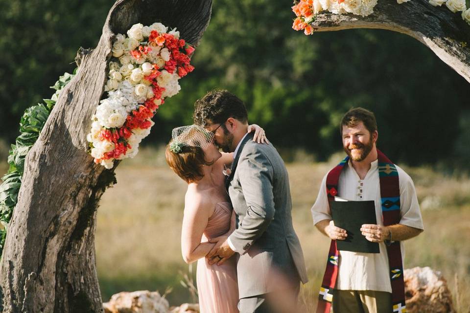 First kiss at outdoor ceremony incorporating be-flowered tree trunks on property.Photo by Nathan Russell Photo.