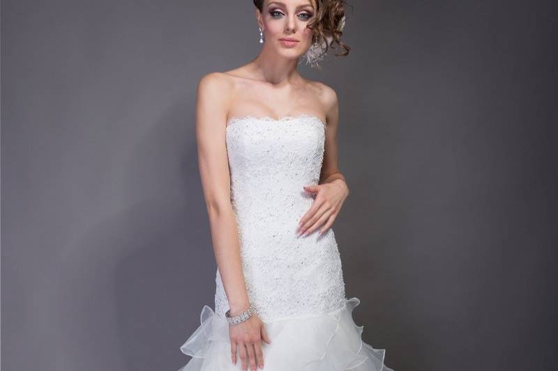 Style “Bernice”Organza.  Dropped waist A-line gown with tiered asymmetric tiered organza ruffled skirt and chapel train.  Strapless slight dip neckline with lace and beaded bodice.