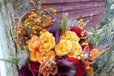 A wonderful fall bouquet of sunset mini callas, chocolate mini callas, various grasses, orange spray roses, Sexy Red roses, guinea fowl feathers and bittersweet vine