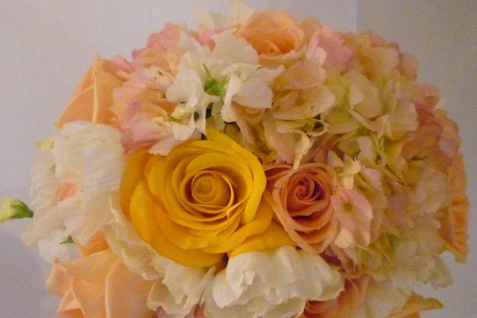 Truly feminine, this bouquet contains small pink garden roses, shell pink peonies, white spray roses, and white stephanotis collared with a variety of patterned and pastel ribbons.