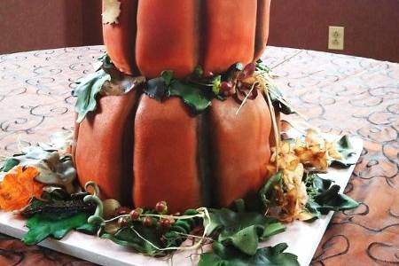 3 pumpkin cakes stacked with gumpaste and fondant leaves and flowers.