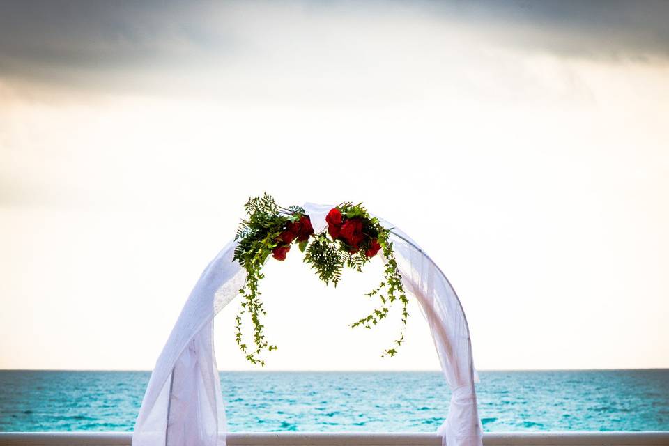 Wedding arch adorned with rose petals. Ceremony is overlooking the ocean as the sky begins to change colors