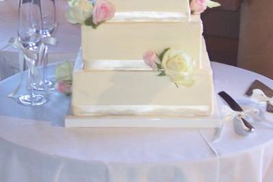4 tiers square cakes stacked with cream and soft pink roses.  Ivory silk ribbon at base of each tier