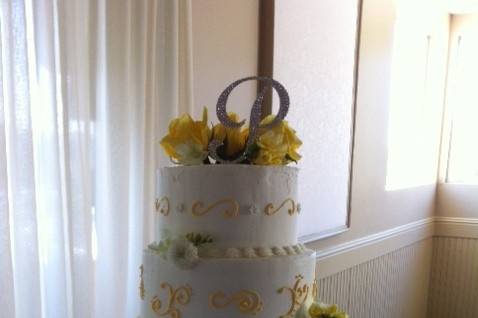 Rustic romance displayed on a stump.  3 buttercream tiers decorated with yellow flowers and a monogrammed silver 