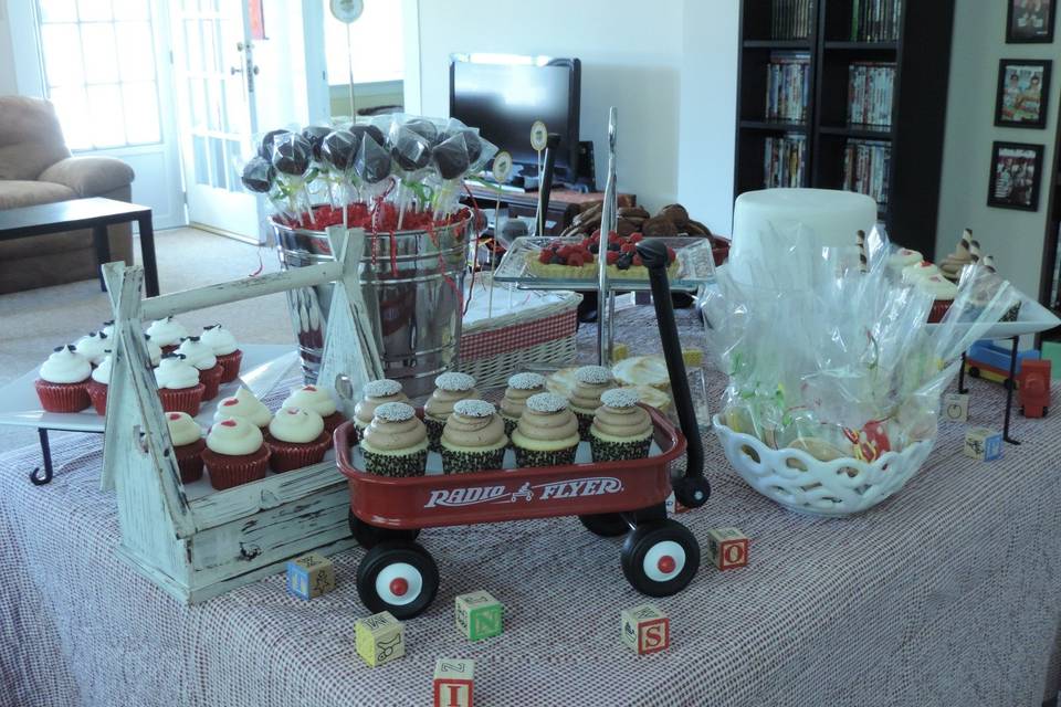 Red wagon holding assorted cupcakes, decorated butter cookies wrapped in cellophane bags, cake pops
