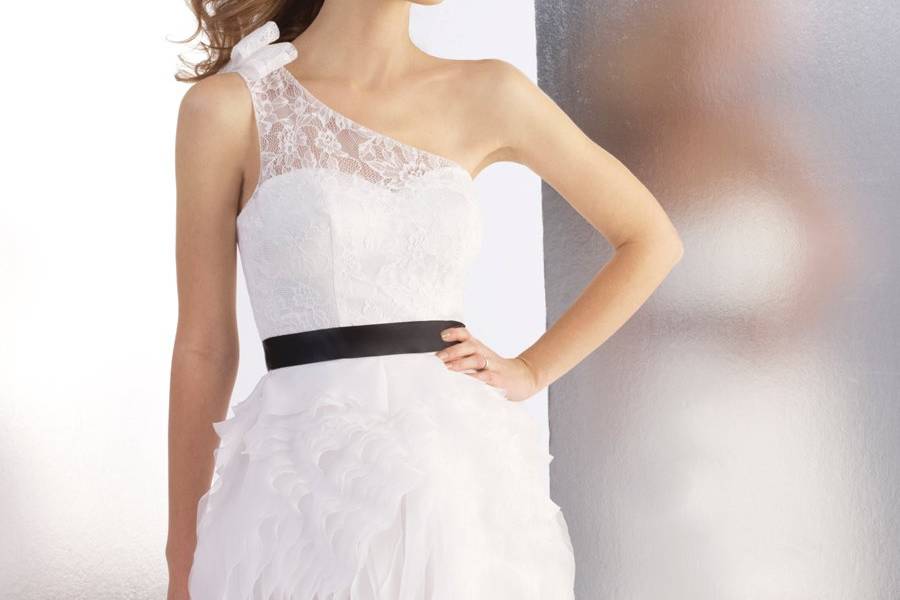Style T540This short a-line features ruffles along the skirt that are arranged into a floral pattern. Chantilly lace adorn the bodice along with an illusion one shoulder. A sash finishes the look.